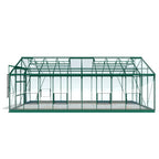 A green, rectangular Rhino Greenhouse with transparent panels stands on a light background. It has a gabled roof and sliding doors on the side, suitable for gardening use.