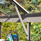 Metal support rod secures Rhino Greenhouse window, surrounded by gardening tools in a sunlit, leafy environment.