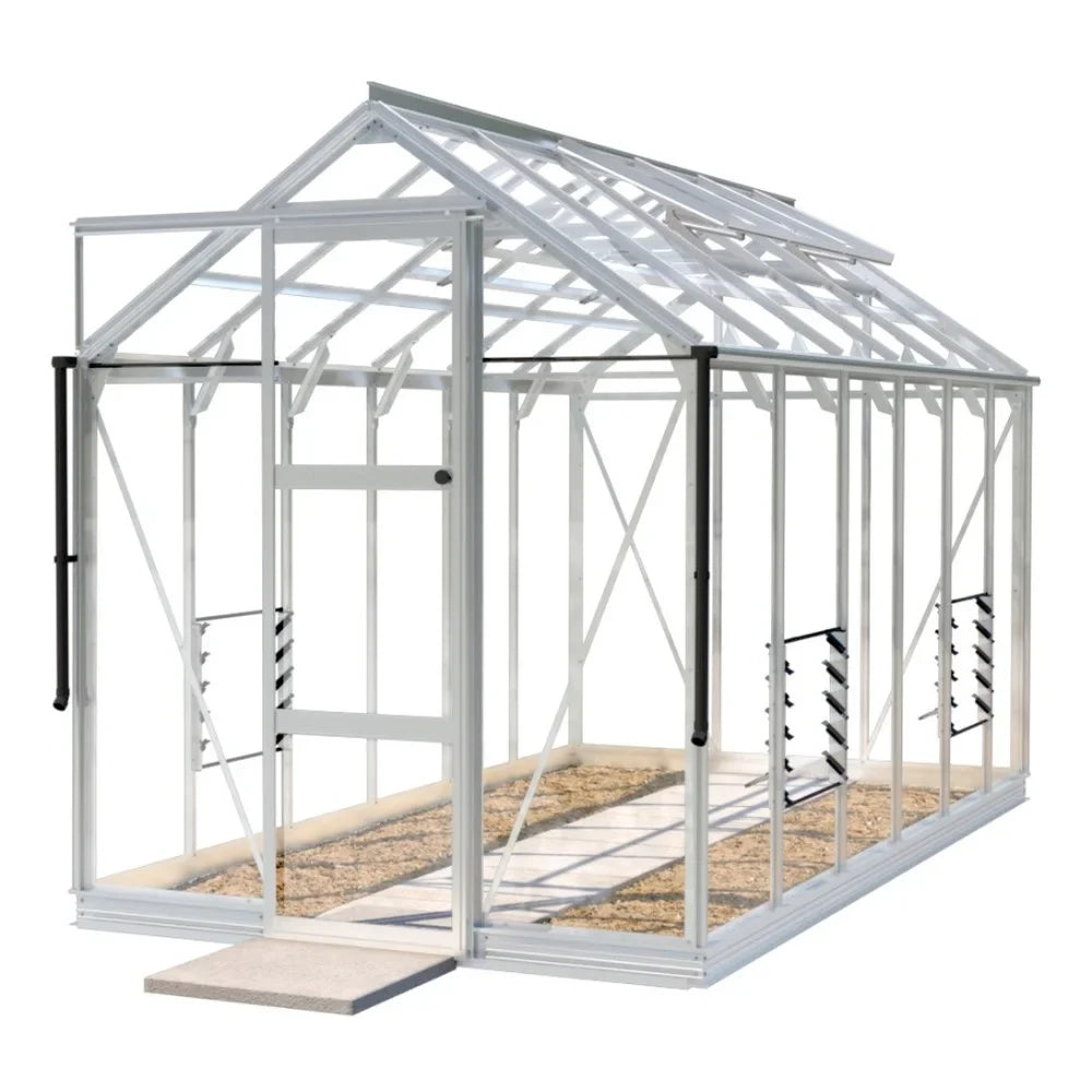 A white-frame Rhino Greenhouse stands with a glass structure, featuring a sliding door and interior shelving, positioned on a concrete base with gravel pathway inside.