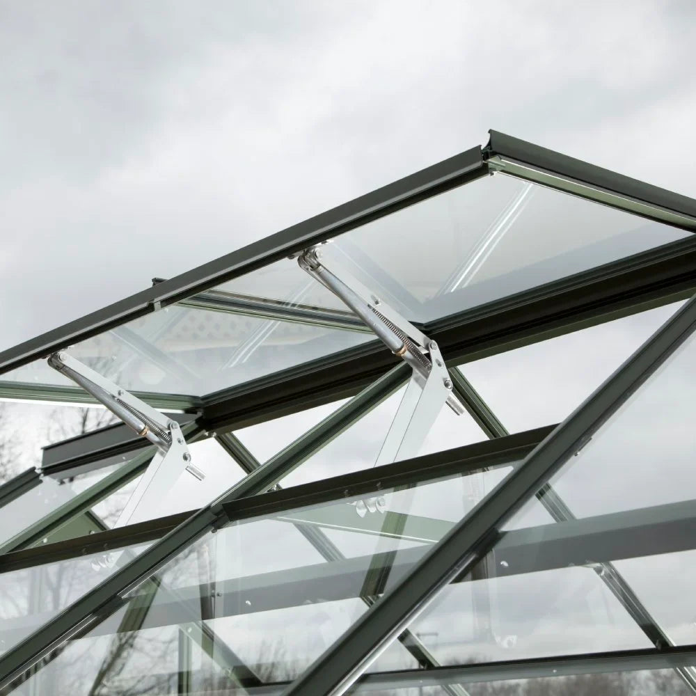 Glass Rhino Greenhouse roof with vent panels slightly open, supported by metal arms; set against a cloudy sky.