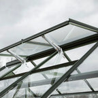 Glass Rhino Greenhouse roof with vent panels slightly open, supported by metal arms; set against a cloudy sky.