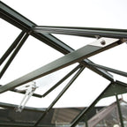 A dark green metal Rhino Greenhouse frame is shown from below, with connected beams and bolts, set against an overcast sky.