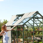 A woman adjusts a Rhino Greenhouse shade, surrounded by plants and gardening tools in a lush outdoor garden setting, with clear blue skies above.